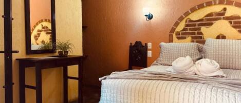 A bedroom with a bed, a bedside table, a mirror, and a wall-mounted light fixture.
