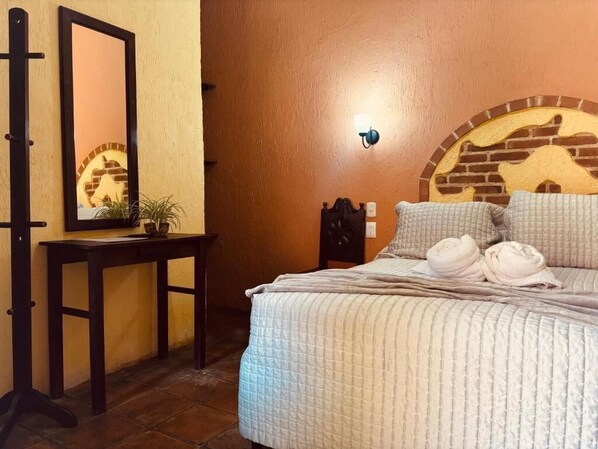 A bedroom with a bed, a bedside table, a mirror, and a wall-mounted light fixture.