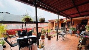 Un patio cubierto con mobiliario exterior, plantas en macetas y vistas de los edificios circundantes.