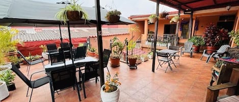 A covered patio with outdoor furniture, potted plants, and a view of the surrounding buildings.