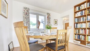 A dining area with a round table, four wooden chairs, a bookshelf, and a window with curtains. - 3 Bed in Keswick (oc-sz007) (Keswick)