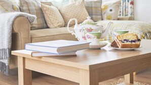 A cozy living room with a sofa, a coffee table with a book and teapot, and a slice of cake. - 3 Bed in Keswick (oc-sz007) (Keswick)