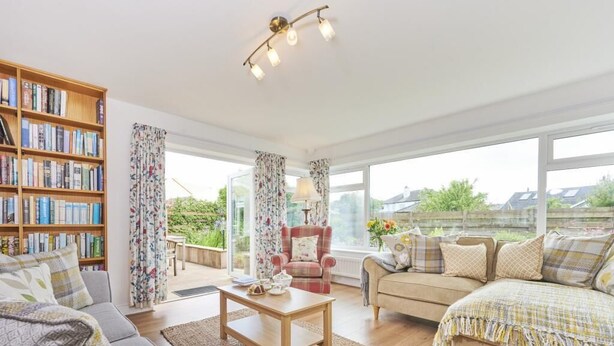 A spacious living room with a large bookshelf, two sofas, a coffee table, and a view of the outdoors through large windows. - 3 Bed in Keswick (oc-sz007) (Keswick)