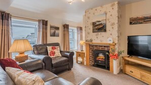 A living room with a fireplace, leather sofa, and a television. - 1 Bed in Keswick (oc-sz166) (Keswick)