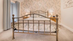 A bedroom with a metal-framed bed, a nightstand with a lamp, a wall with a floral pattern, and a ceiling light fixture. - 1 Bed in Keswick (oc-sz166) (Keswick)