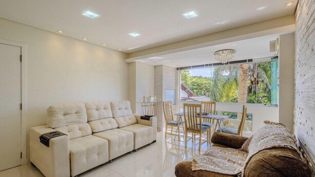 A modern living room with a sofa, a dining table with chairs, and a view of greenery outside. - Beautiful Apt 450m From Lagoa da Conceicao Crm0201 (Florianópolis)