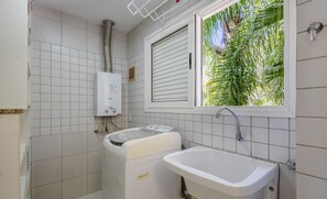 A bathroom with white tiles, a window with blinds, a sink, and a washing machine. - Beautiful Apt 450m From Lagoa da Conceicao Crm0201 (Florianópolis)