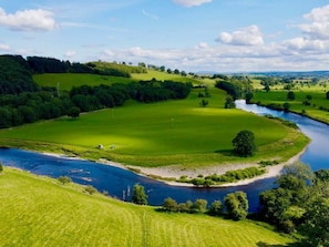 Ein Fluss schlängelt sich durch eine üppige, grüne Landschaft mit sanften Hügeln und blauem Himmel.