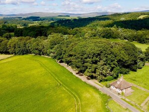 Van bovenaf een landelijk landschap, met een huis omringd door velden en dicht bos.