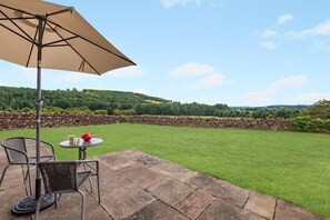 Eine Terrassenfläche mit Tisch und Stühlen, einem Sonnenschirm und einer Steinmauer im Hintergrund.