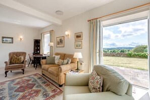 Ein Wohnzimmer mit Sofa, Sessel und Esstisch. Durch ein großes Fenster ist Gartenblick.