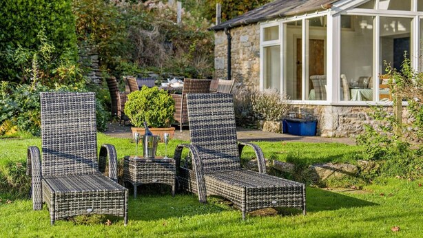 A garden with wicker chairs, a stone building with a large window, and a table with a potted plant. - 4 Bed in Sedbergh (oc-sz595) (Millthrop)