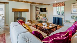 A cozy living room with a fireplace, a television, a bookshelf, and a window with a view. - 4 Bed in Sedbergh (oc-sz595) (Millthrop)