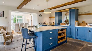 A kitchen with blue cabinets, a central island, and a dining area with plaid chairs. - 4 Bed in Sedbergh (oc-sz595) (Millthrop)