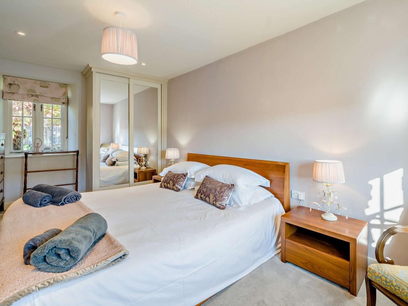 A bedroom with a large bed, bedside tables, a mirror, and a window.
