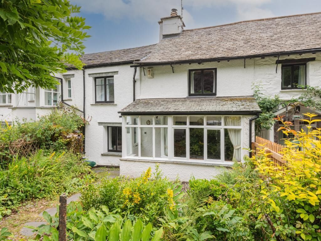 A white building with a tiled roof, a covered porch, and a garden with various plants.