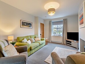 Ein Wohnzimmer mit einem grünen Sofa, einem braunen Sessel, einem Flachbildfernseher, einer Lampe und einem Bild an der Wand.