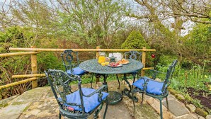 Un área de comedor al aire libre con una mesa redonda y cuatro sillas, rodeada por una valla de madera y follaje.