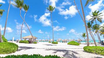 A beach with palm trees, a thatched-roof structure, and a clear blue sky.