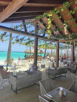 Un espacio al aire libre con mobiliario de mimbre, una terraza de madera y vistas a la playa y el océano.