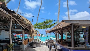 Un bar en la playa con mesas al aire libre, palmeras y vista al océano.