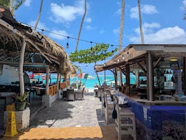 Un bar en la playa con mesas al aire libre, palmeras y vista al océano.