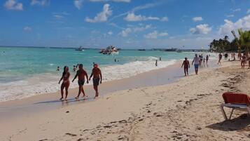 Uma praia com pessoas caminhando pela margem, barcos na água e um céu claro.