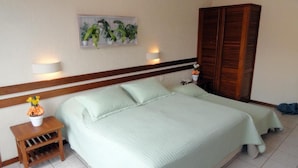 A bedroom with a bed, bedside tables, a nightstand, a wall-mounted lamp, a wooden wardrobe, and a framed picture on the wall. - Village du Soleil (Cabo Frio)
