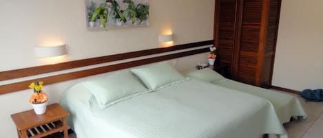 A bedroom with a bed, bedside tables, a nightstand, a wall-mounted lamp, a wooden wardrobe, and a framed picture on the wall.