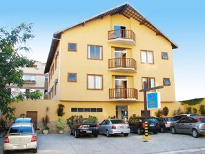 A multi-story yellow building with a balcony on the second floor, a parking lot with several cars, and a sign indicating a hotel.
