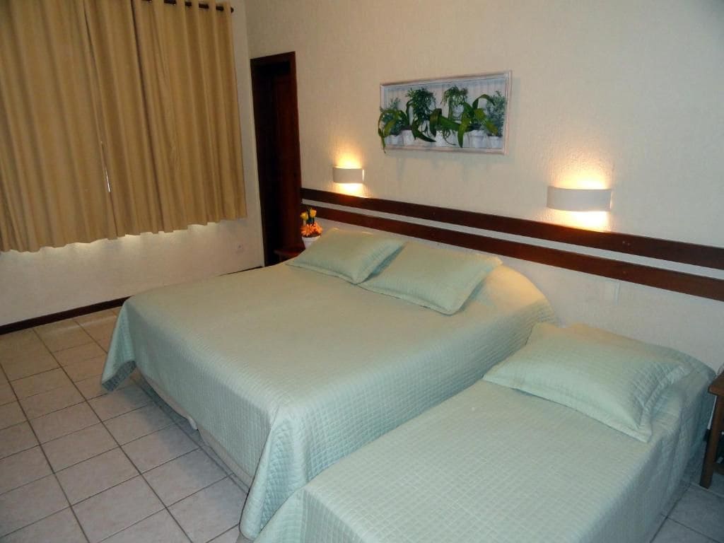Habitación de hotel con dos camas, una lámpara de pared, una puerta y un cuadro con plantas.