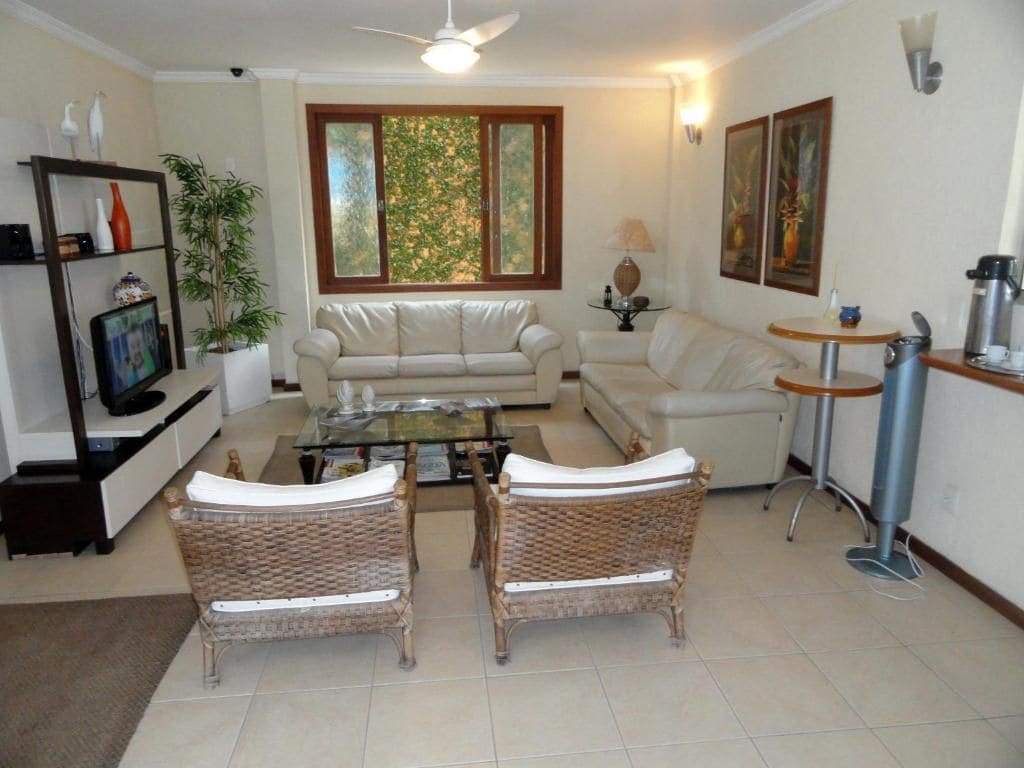 Ein Wohnzimmer mit einer Couch, zwei Korbstühlen, einem Couchtisch, einem Fernseher, einem Bücherregal, einem Fenster mit Blick und einer Wandlampe.