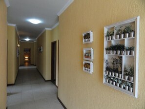A hallway with a tiled floor, a light fixture on the ceiling, and a wall-mounted shelf with potted plants.