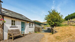 A white building with a blue door, a wooden bench, and a stone wall in a rural setting. - 1 Bed in Cockermouth (oc-sz160) (Lorton)