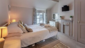 Een slaapkamer met een bed, nachtlampjes, een dressoir, een spiegel, een open haard en een televisie aan de muur.