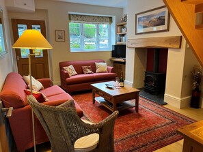 A living room with a sofa, a chair, a coffee table, a lamp, a fireplace, and a bookshelf. - 2 Bed in Ambleside (oc-sz451) (Ambleside)