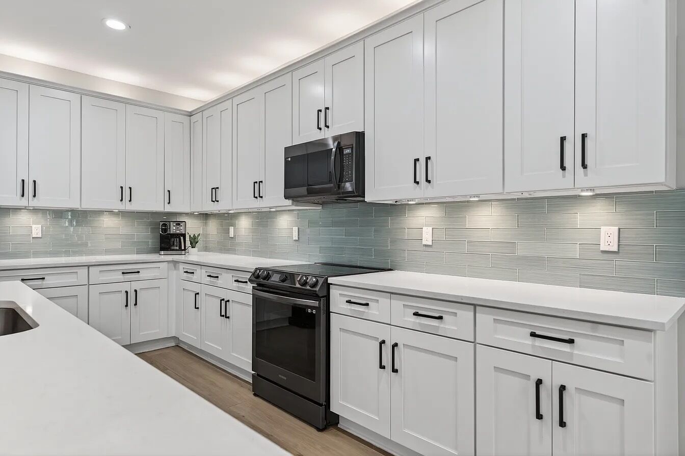 Une cuisine moderne avec des meubles blancs, un micro-ondes noir et une cuisinière.