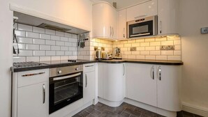 A modern kitchen with white cabinets, a built-in oven, a microwave, and a tiled backsplash. - 3 Bed in Keswick (oc-sz118) (Keswick)