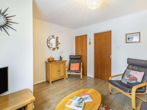 A living room with a sofa, a chair, a coffee table with magazines, a TV, a wooden cabinet, a mirror, and a door. - 2 Bed in Keswick (oc-sz462) (Keswick)
