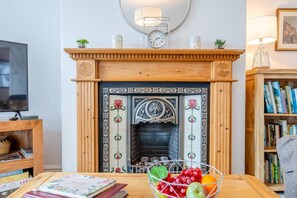 Ein Wohnzimmer mit Kamin, Fernseher, Bücherregal und einem Tisch mit Obstschale.