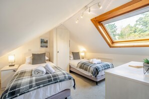 Ein Schlafzimmer mit zwei Betten, einem kleinen Schreibtisch und einem Fenster mit Blick auf Bäume.