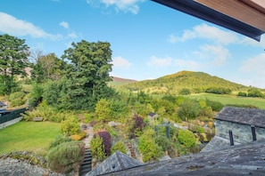 Ländliche Landschaft mit Blick auf einen Hügel, ein Garten mit verschiedenen Pflanzen und ein kleines Gebäude.