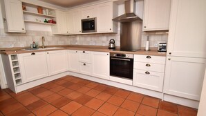 Una cocina con gabinetes blancos, una campana extractora de acero inoxidable, un microondas y un horno.