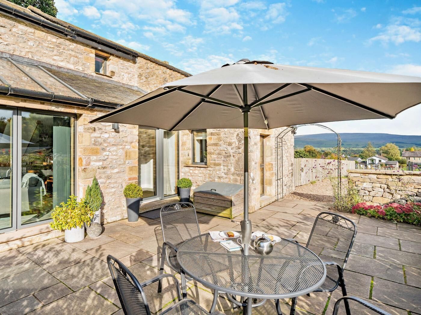 A patio with a table and chairs, an umbrella, and a stone building with a view.