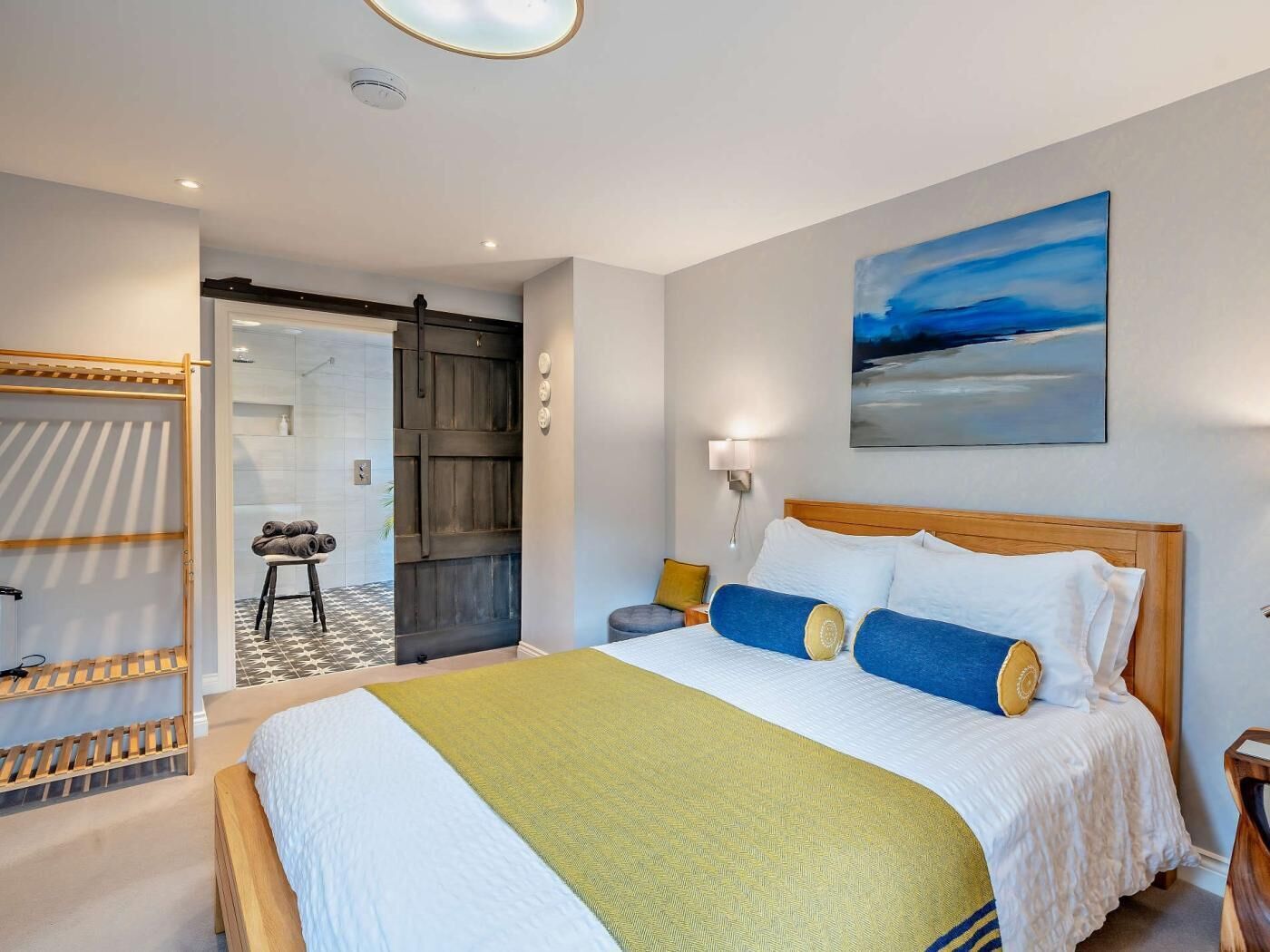A bedroom with a bed, a painting, and a view of the bathroom.