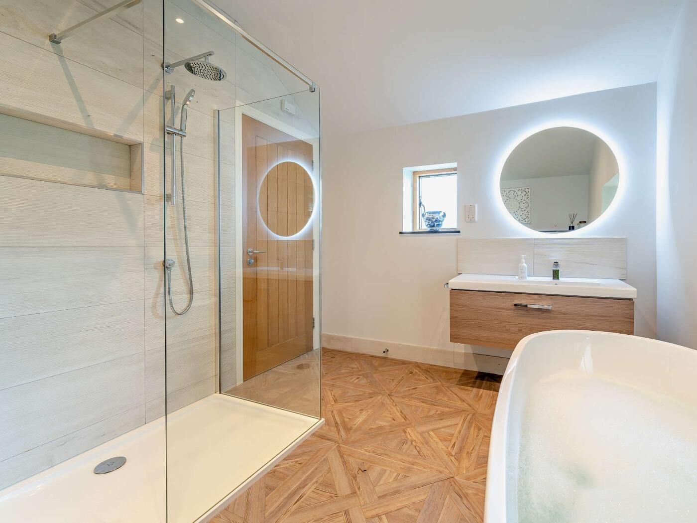 A modern bathroom with a glass shower enclosure, a freestanding bathtub, and a vanity with a round mirror.
