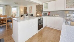 Eine moderne Küche mit weißen Schränken, einer zentralen Kochinsel, einer Wand mit Steinverkleidung und einem Essbereich mit Holzmöbeln.