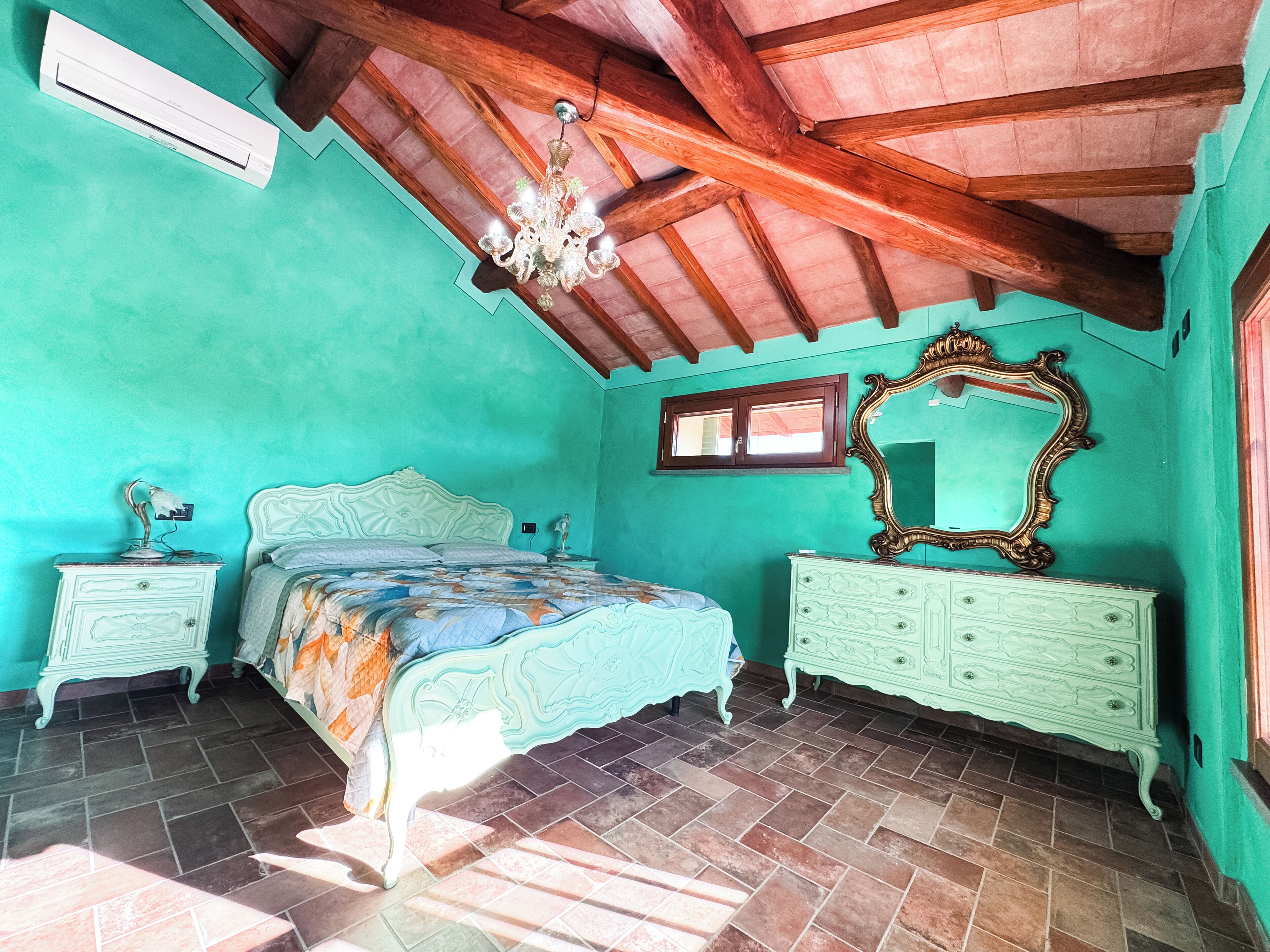 A bedroom with a bed, a dresser, a mirror, a chandelier, and a window.