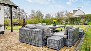 Ein Patio-Bereich mit Korbmöbeln, einem Tisch und einem Garten im Hintergrund.