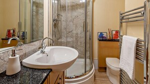 Een badkamer met een douchecabine van gebogen glas, een witte wastafel en een toilet.